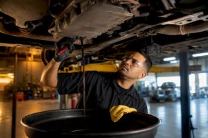 Technician draining transmission fluid beneath vehicle