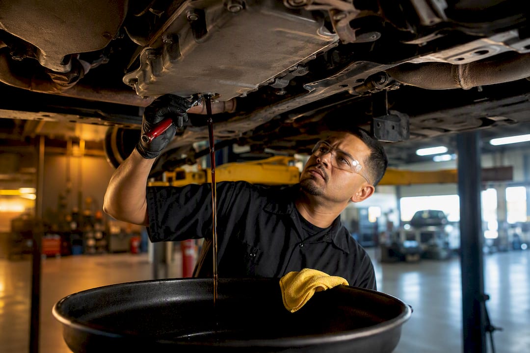 Technician draining transmission fluid beneath vehicle