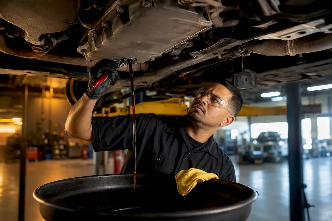 Technician draining transmission fluid beneath vehicle